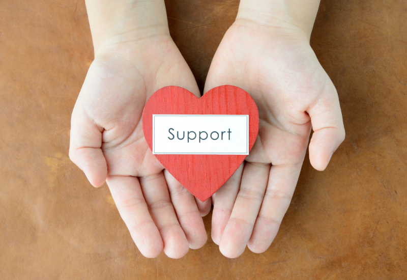 Hands holding a red heart with the word “Support.”
